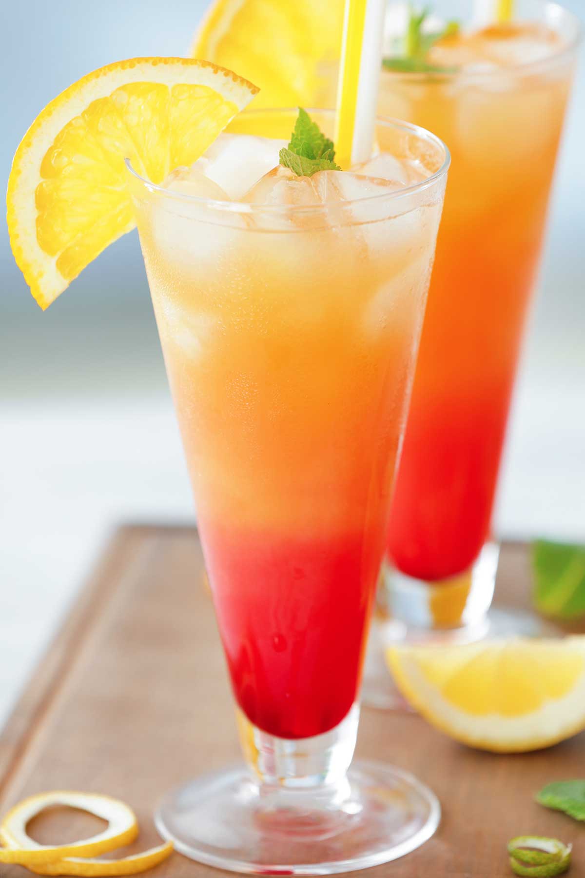 red and orange tequila mezcal sunrise in a glass with lemon wedges
