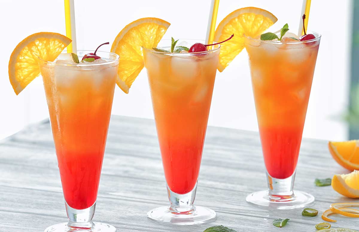 three red and orange tequila sunrises in a glasses with orange wedges