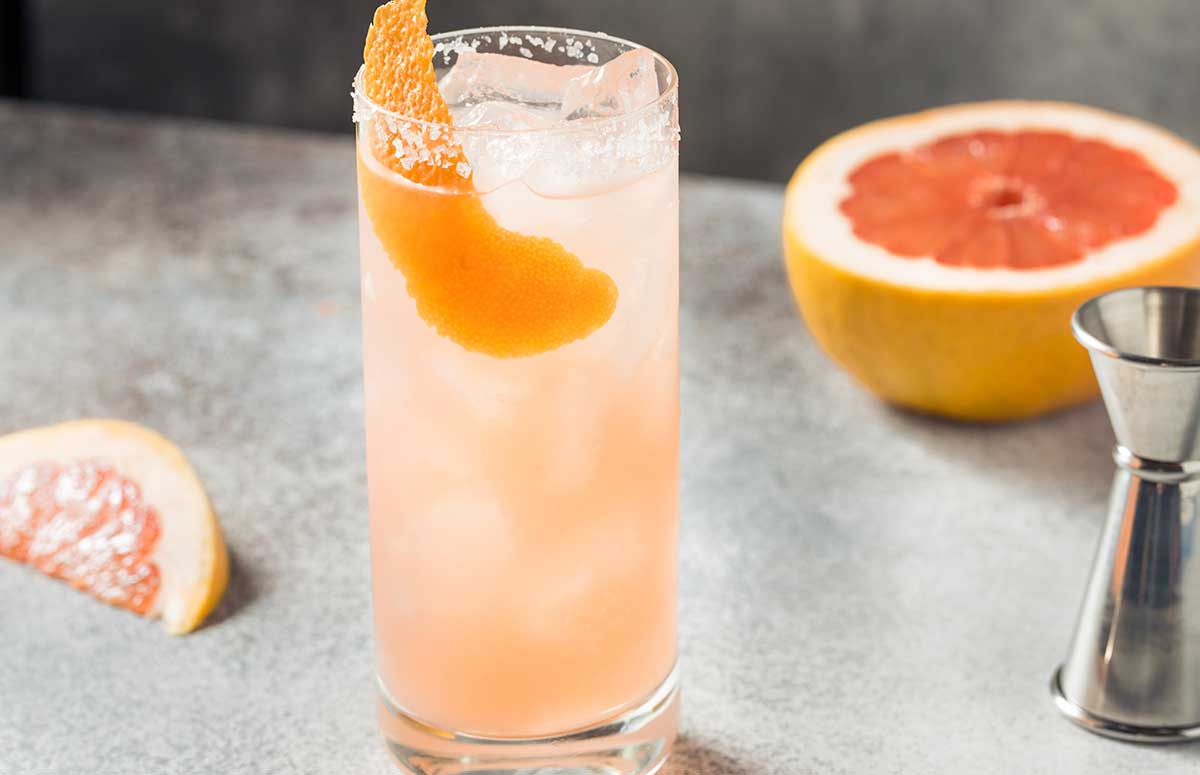 a glass of mezcal paloma and one grapefruit on the side. 