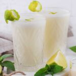 two tall glasses with coconut lime margarita with lime wedges on the side