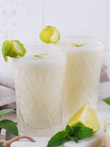 two tall glasses with coconut lime margarita with lime wedges on the side