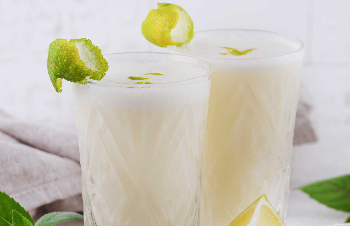 two tall glasses with coconut lime margarita with lime wedges on the side