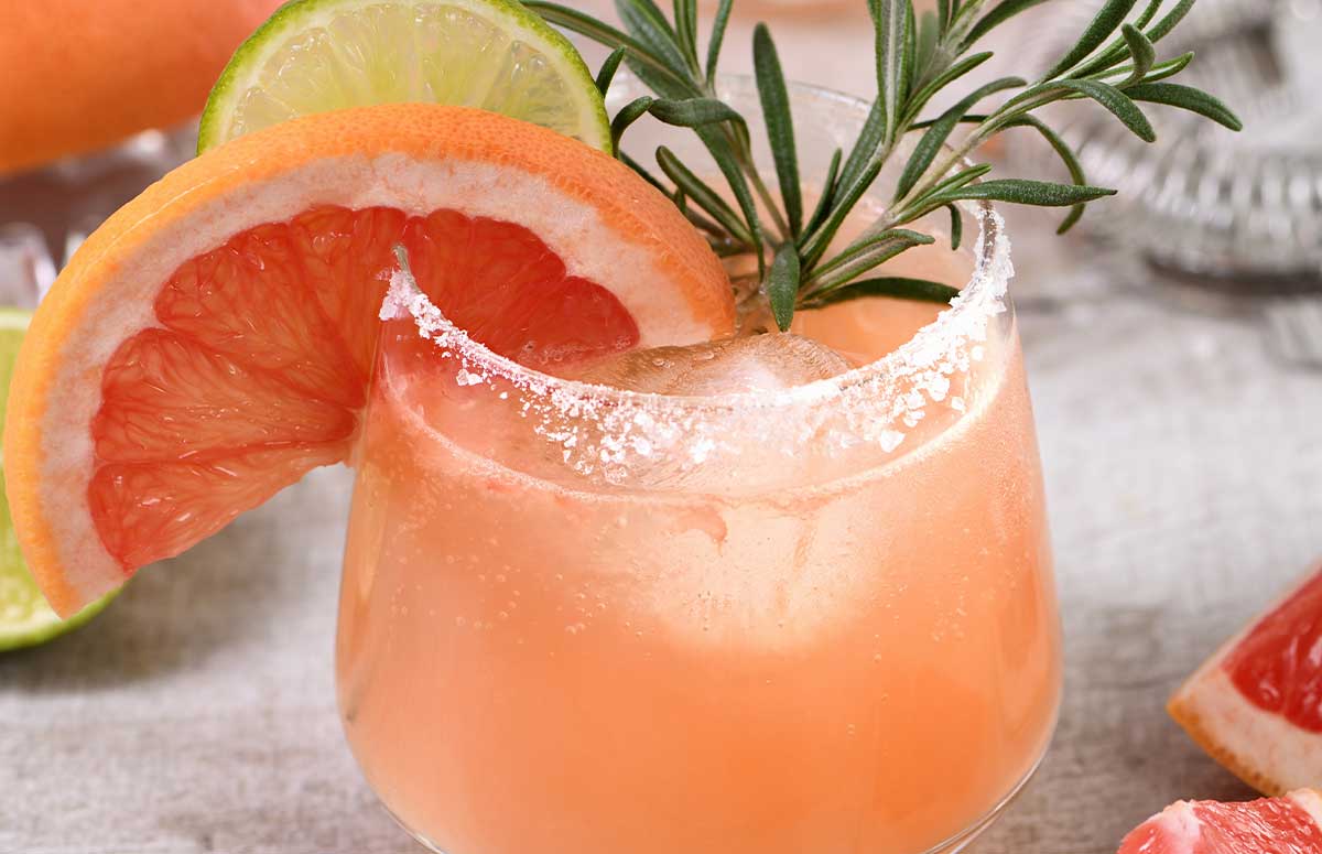 a glass of mezcal paloma and one grapefruit on the side. 