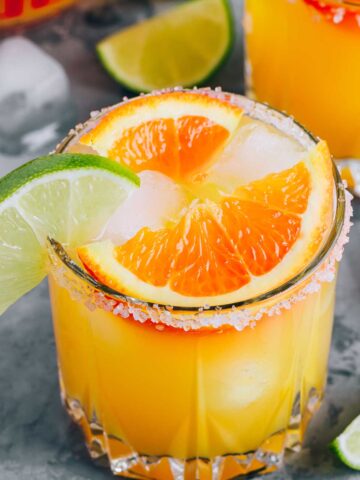 a glass of orange margarita with orange and lime wedges on the rim