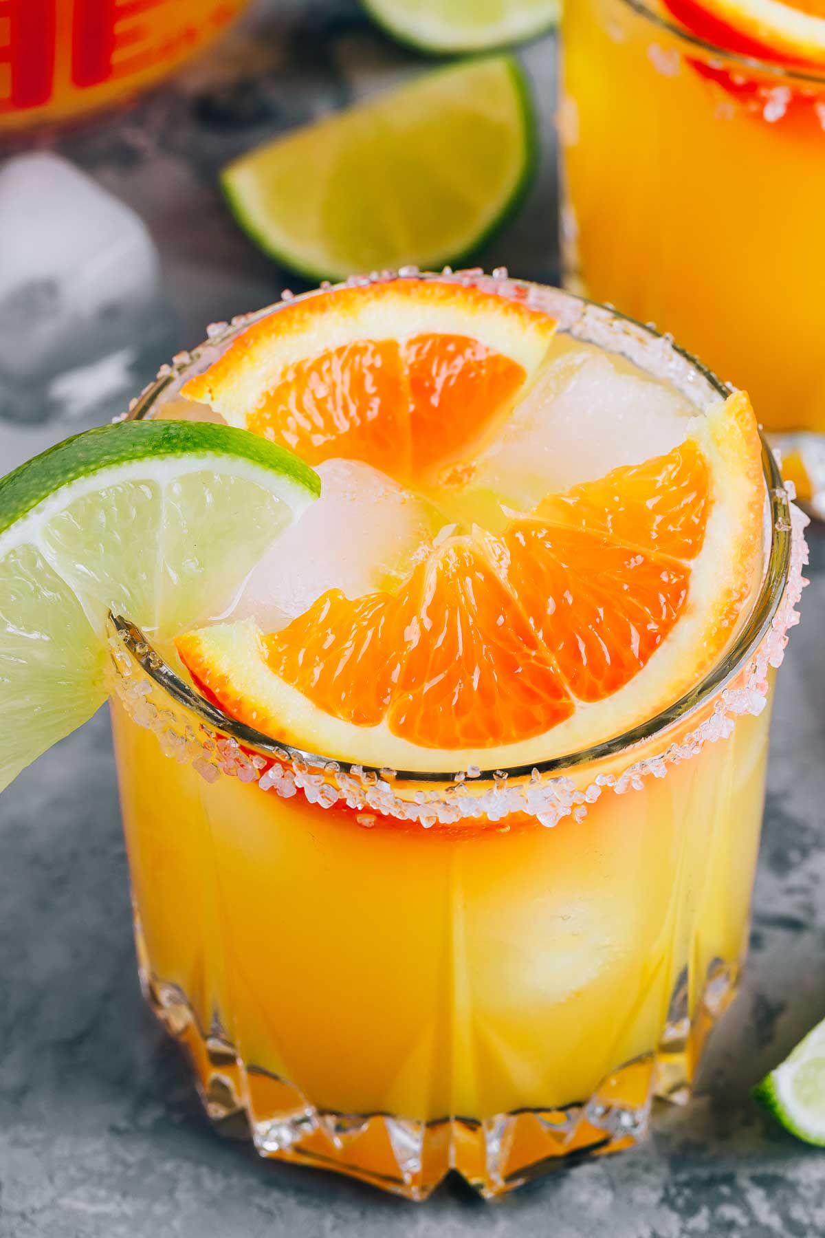 a glass of orange margarita with orange and lime wedges on the rim