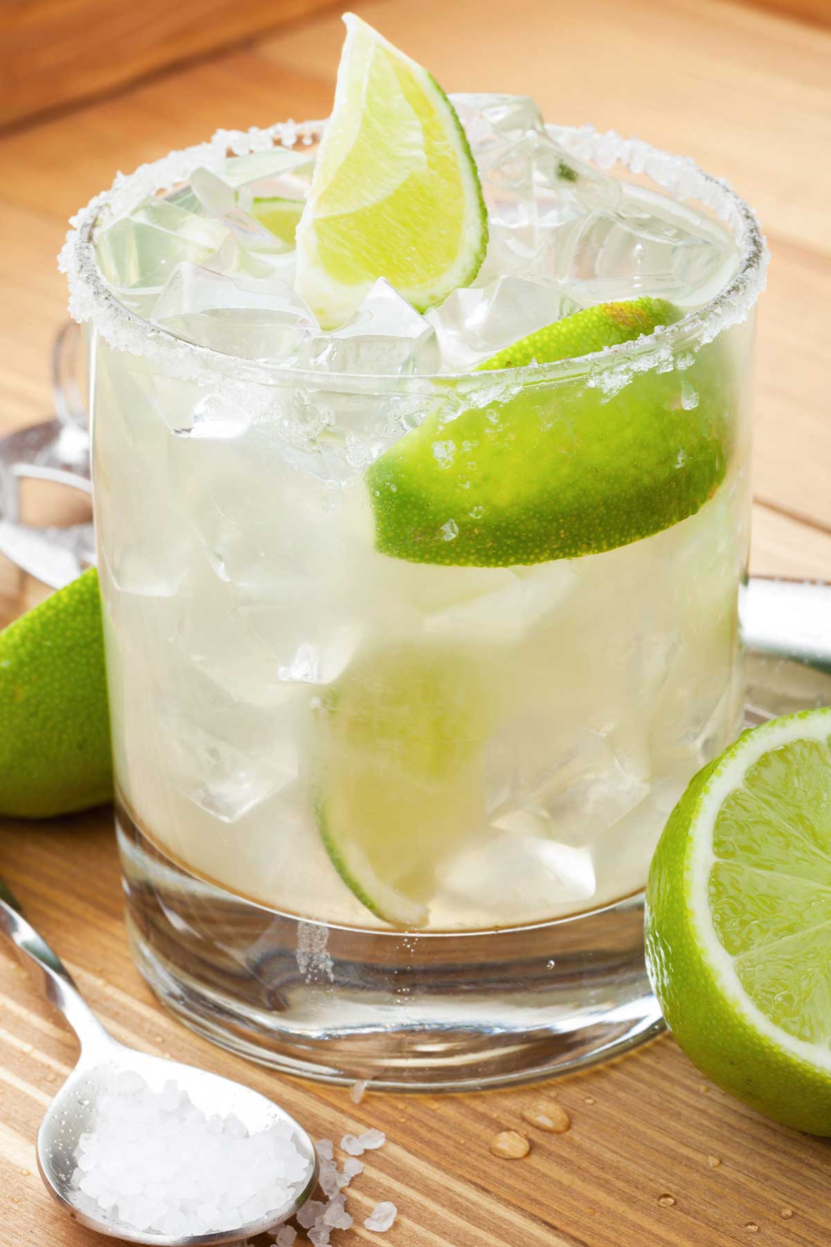Low-calorie margarita in a salt rimmed glass with wedges of lime, fresh whole  lime sliced on wooden countertop.