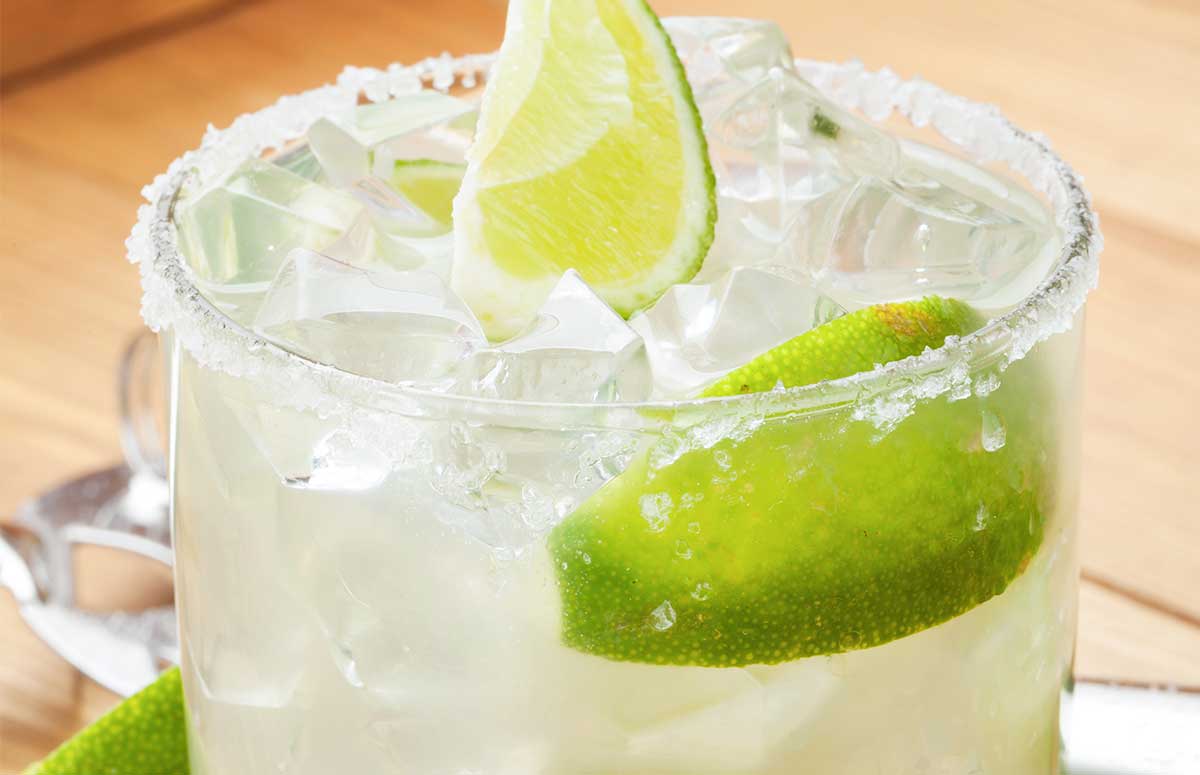 Close up of low-calorie margarita in a salt-rimmed glass with lime wedges.