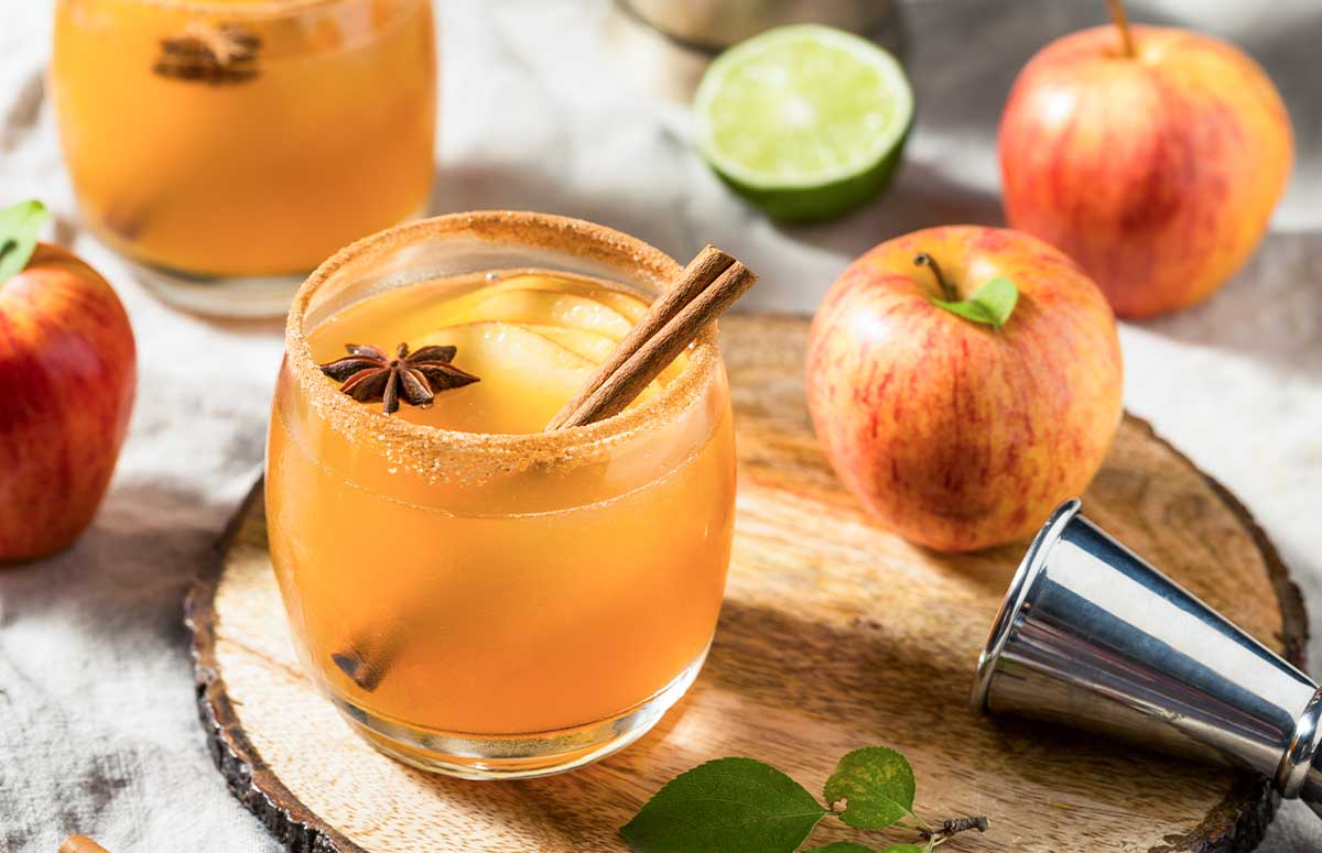 Apple Pie Margarita in a glass rimmed with cinnamon sugar and garnished with a cinnamon stick and sliced apples.