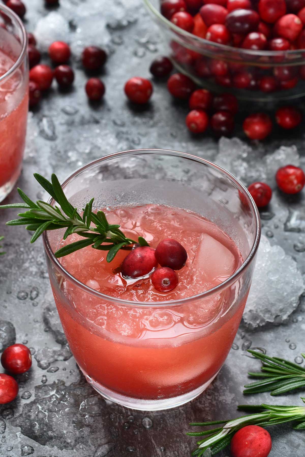 Glass of cranberry margarita with fresh cranberries and a rosemary sprig for garnish, bowl of fresh cranberries in the background.