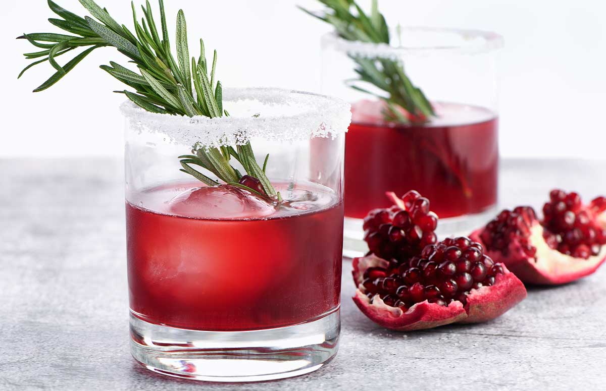 two small glasses of pomegranate margarita with garnishes