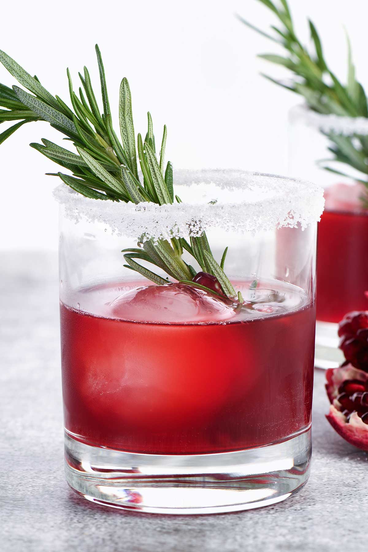 closeup of pomegranate margarita in a glass with rosemary garnish