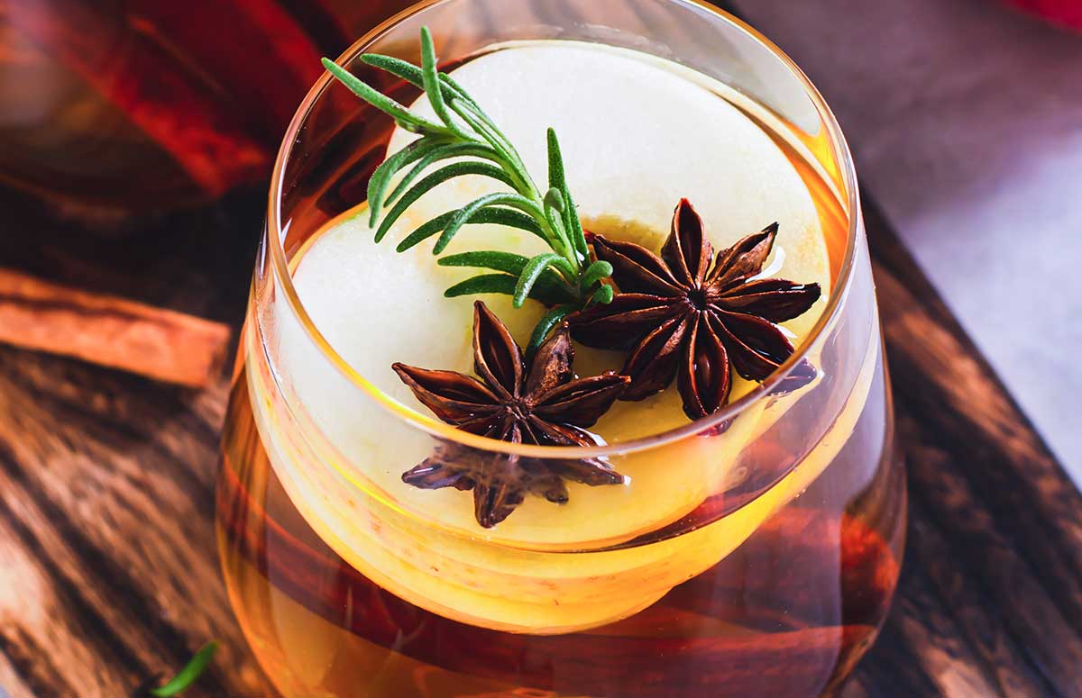Close up of a Spiced Apple Margarita with sliced apple, star anise cloves, and a sprig of rosemary.
