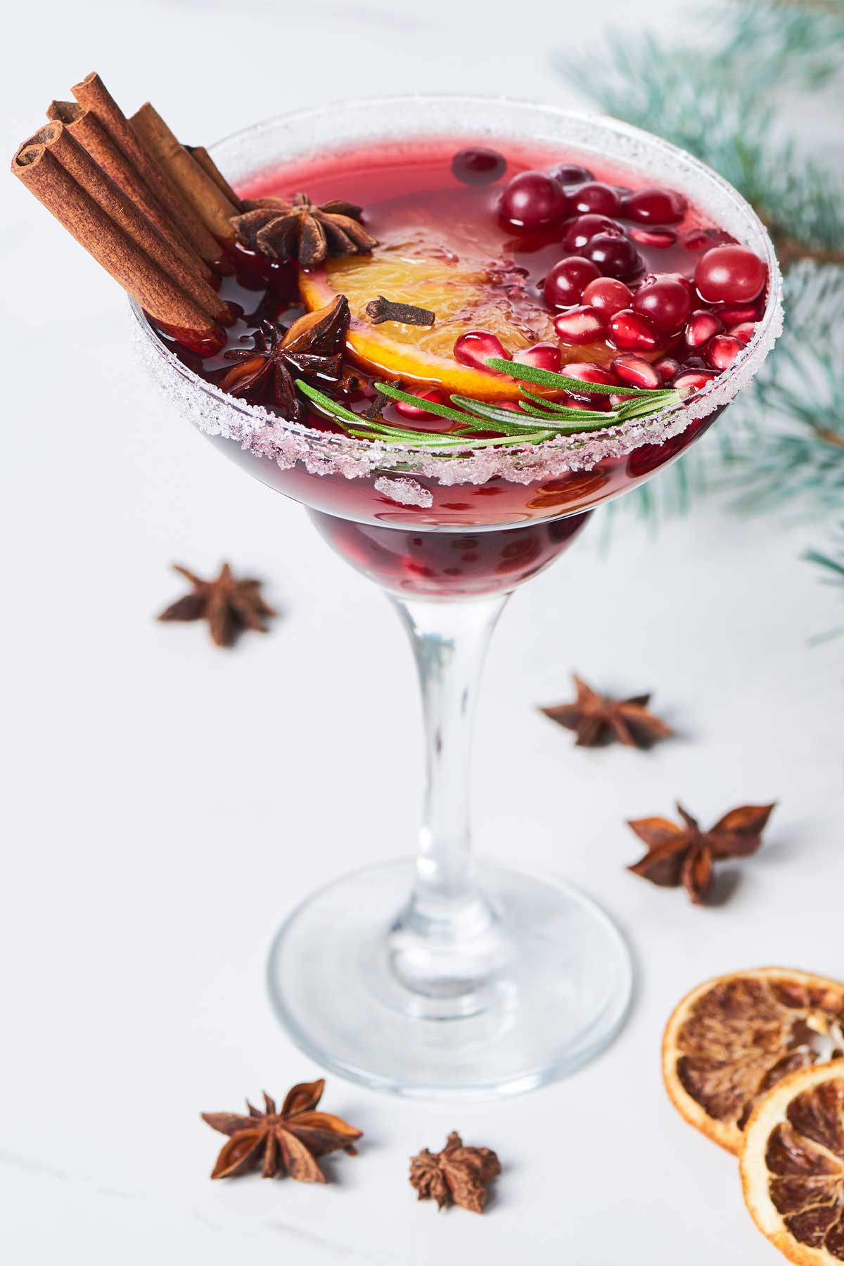 glass of a Christmas margarita garnished with cinnamon sticks, pomegranate, and dehydrated oranges. 