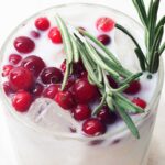 closeup of a white margarita topped with cranberries and rosemary