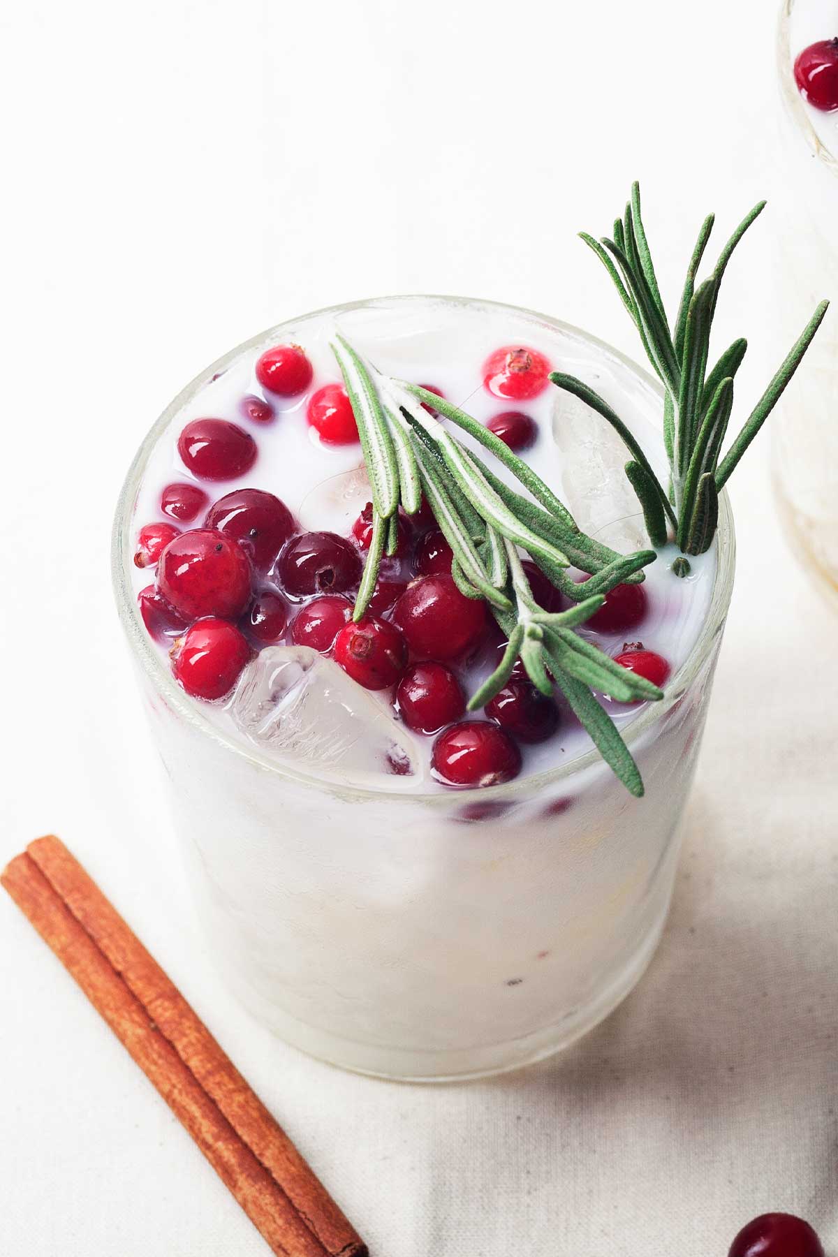closeup of a white margarita topped with cranberries and rosemary