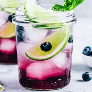 Small mason jar of blueberry margarita with a lime wedge on top
