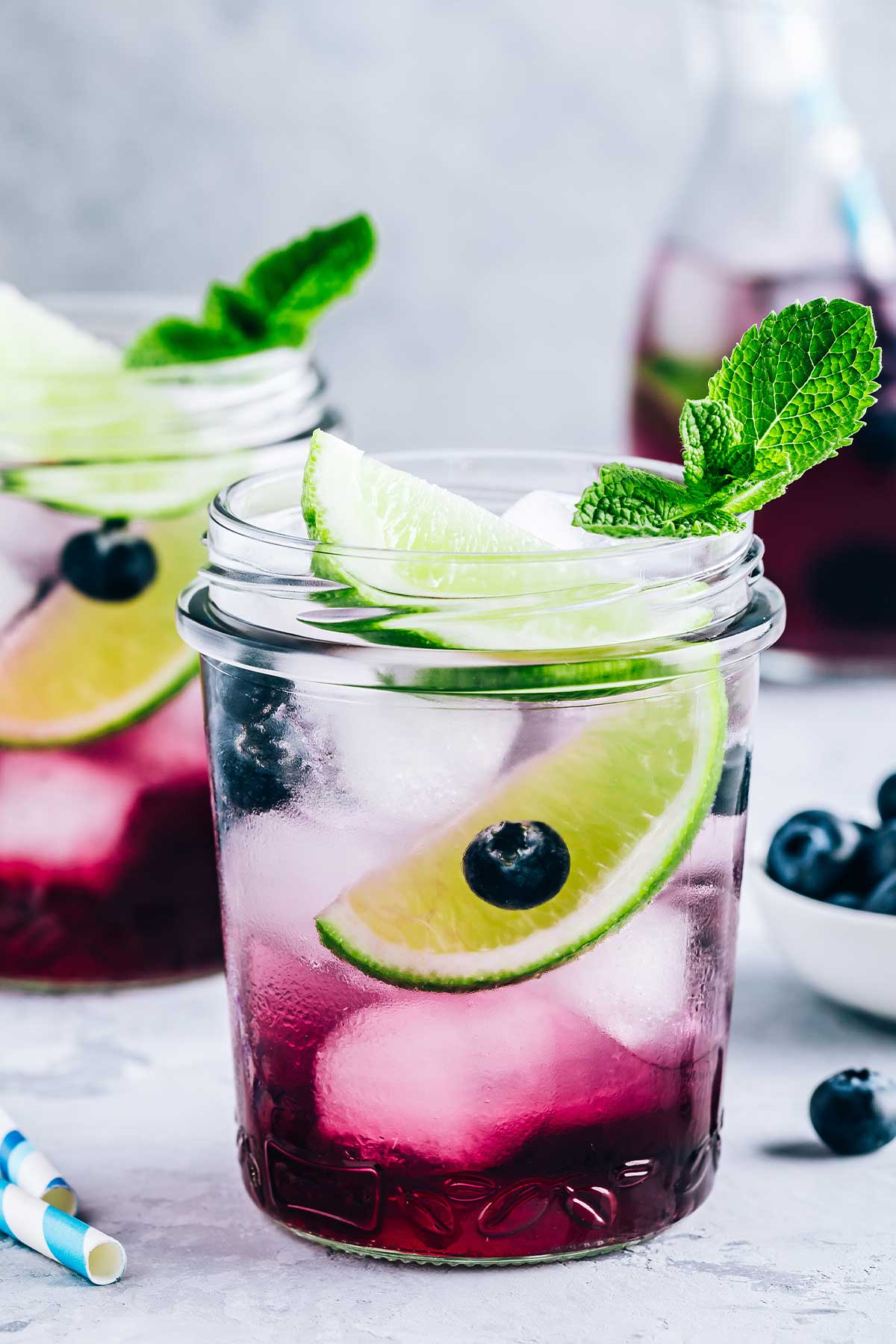 two mason jar glasses of blueberry margaritas with lime wedges and garnishes