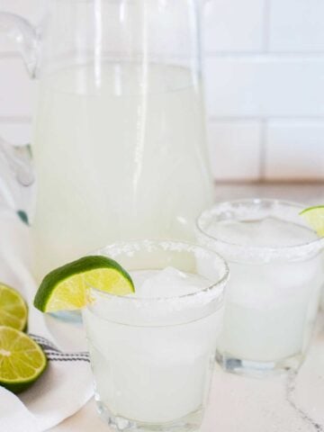 a pitcher of margaritas with two glasses filled with margaritas