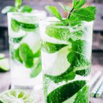 two glasses filled with a tequila mojito cocktail and mint leaves