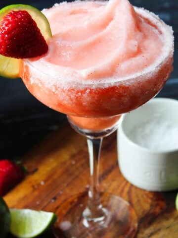 A frozen strawberry margarita rimmed with salt and garnished with a strawberry and lime