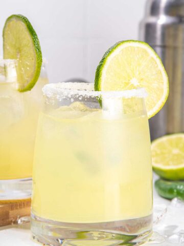 A margarita glass with a salted rim and a lime wedge filled with Mezcal margarita in it