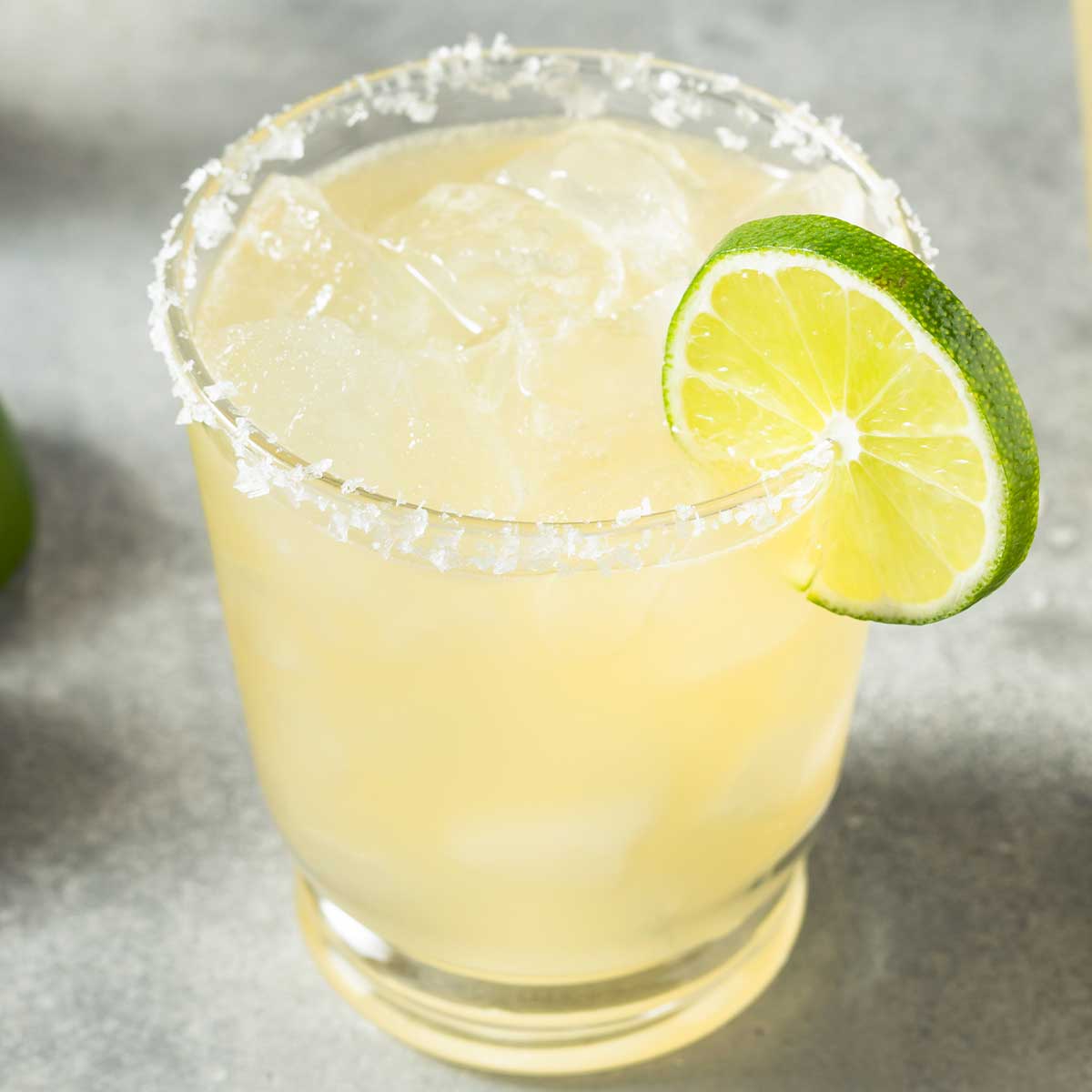 A margarita glass with a salted rim with a margarita mix and a lime wedge on the side