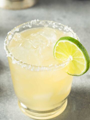 A margarita glass with a salted rim with a margarita mix and a lime wedge on the side