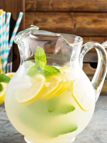 A pitcher filled with lemonade & tequila with lemon slices and mint