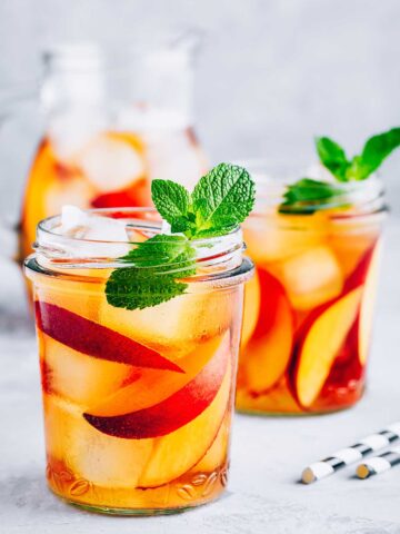 two glasses of tequila peach lemonade with sliced peaches
