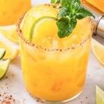 Skinny Orange Margarita with Tajin rim, orange and lime slices, and mint sprig.