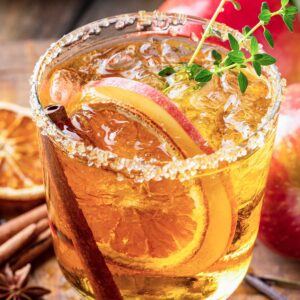 Skinny Thanksgiving Margarita with sugared rim, cinnamon sticks, apple slices, dried oranges, and a green garnish.