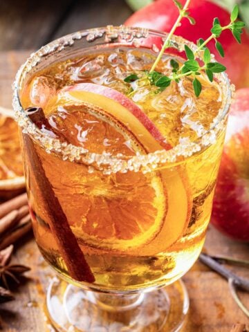 Skinny Thanksgiving Margarita with sugared rim, cinnamon sticks, apple slices, dried oranges, and a green garnish.