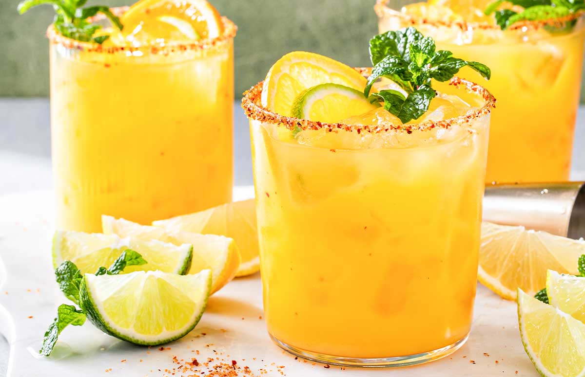 three orange mezcalita glasses with lime wedges