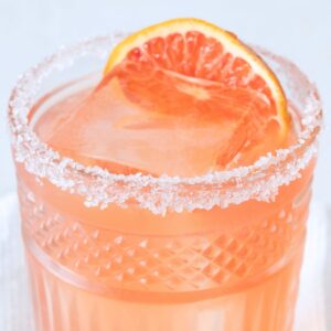 skinny blood orange margarita in a low ball glass with a salted rim and a blood orange slice