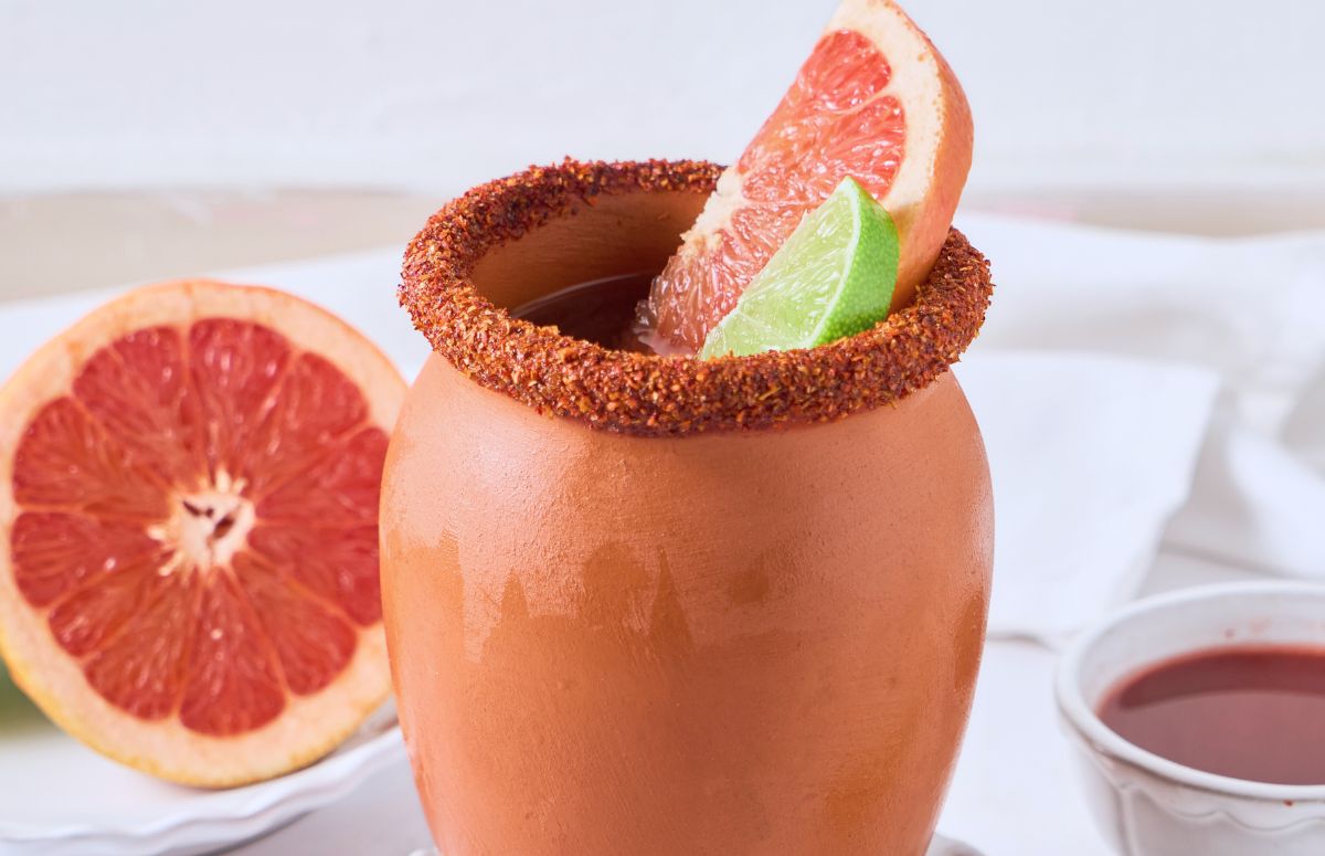 A cantarito with a tajin rim, grapefruit and lime wedges