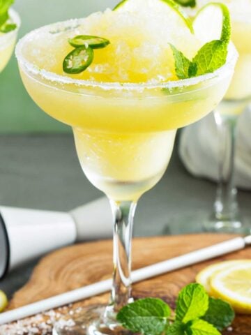 Spicy Frozen Margarita with a salted rim and lime slices and jalapeno rounds