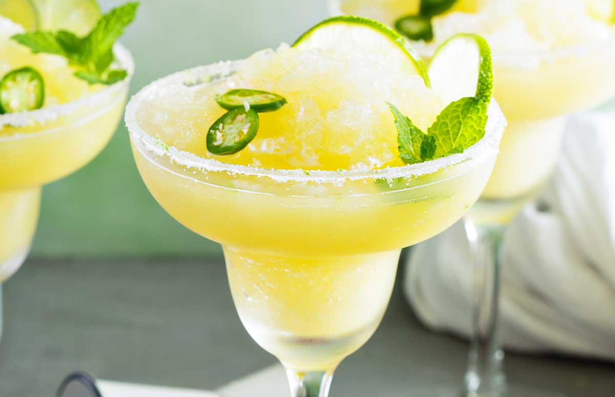 Spicy Frozen Margarita with a salted rim and lime slices and jalapeno rounds