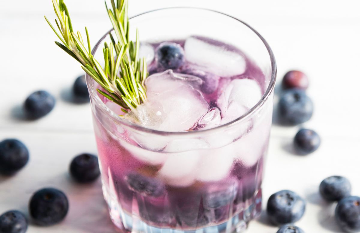 glass of a blueberry cocktail with blueberries scattered on the countertop