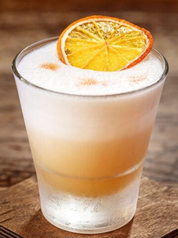 cinnamon tequila sour topped with foam and an orange slice