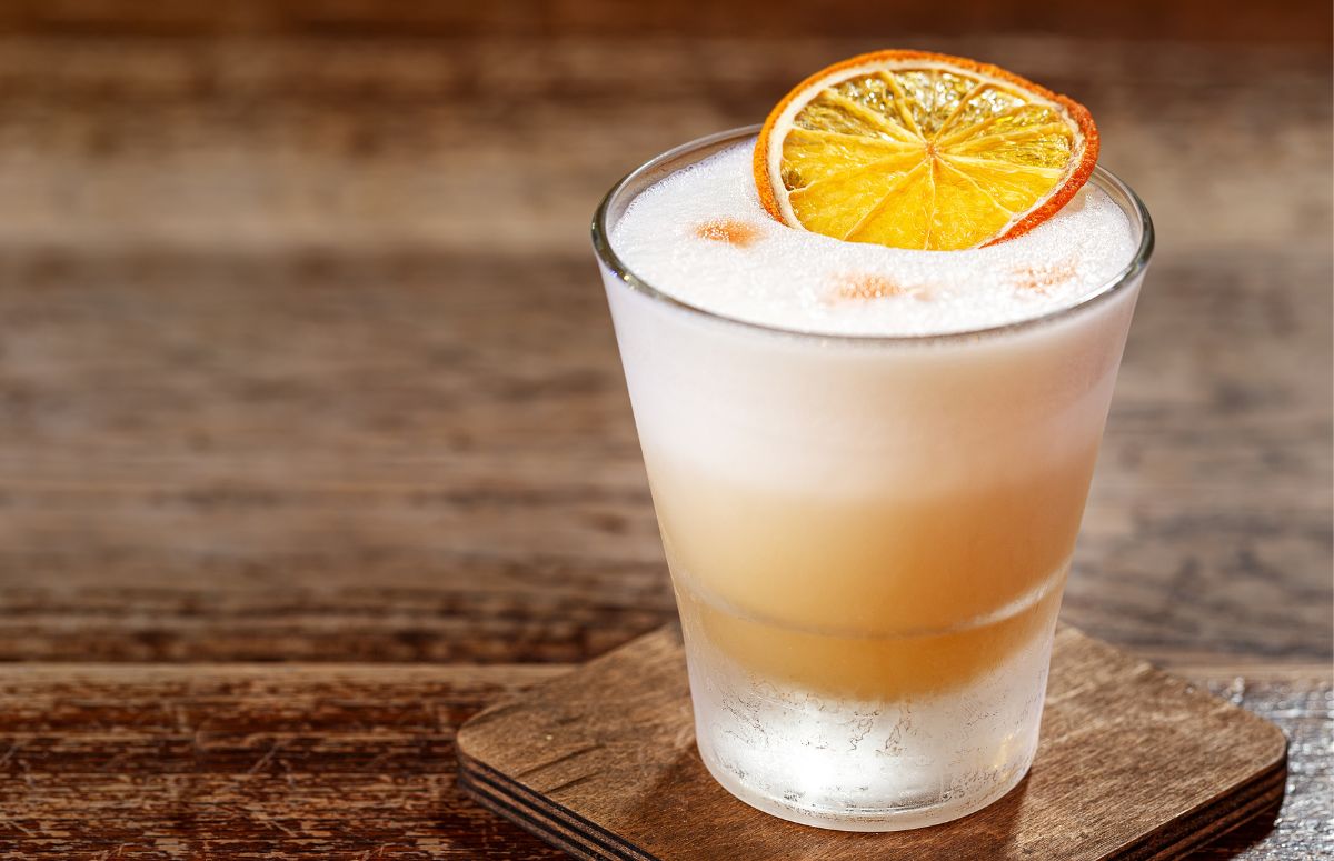 cinnamon tequila sour with foam topped with a slice of orange