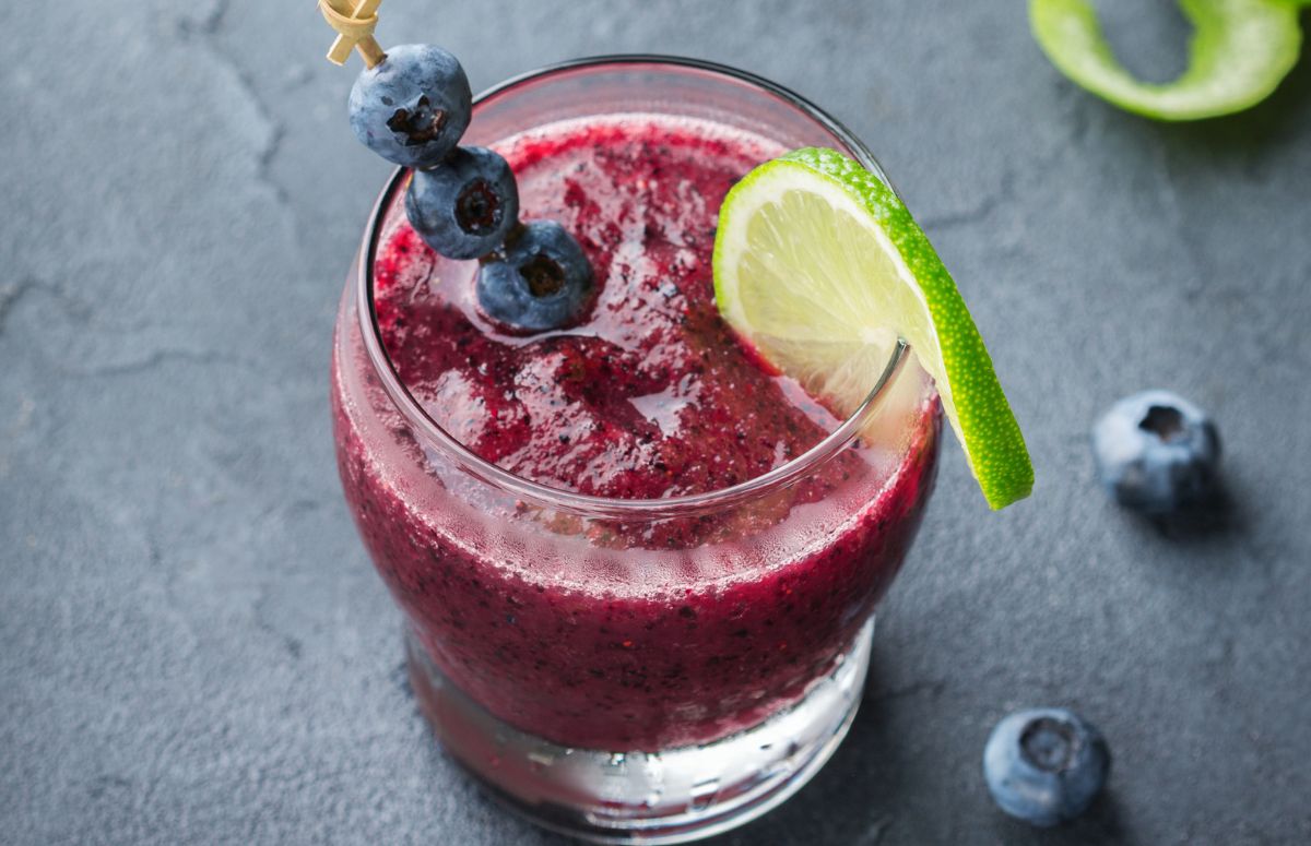 glass of frozen margarita garnished with blueberries and a slice of lime