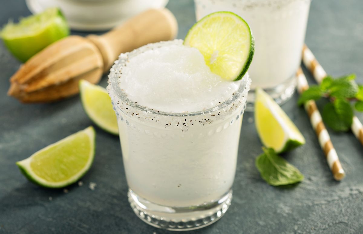 two frozen margaritas in glasses with lime wedges