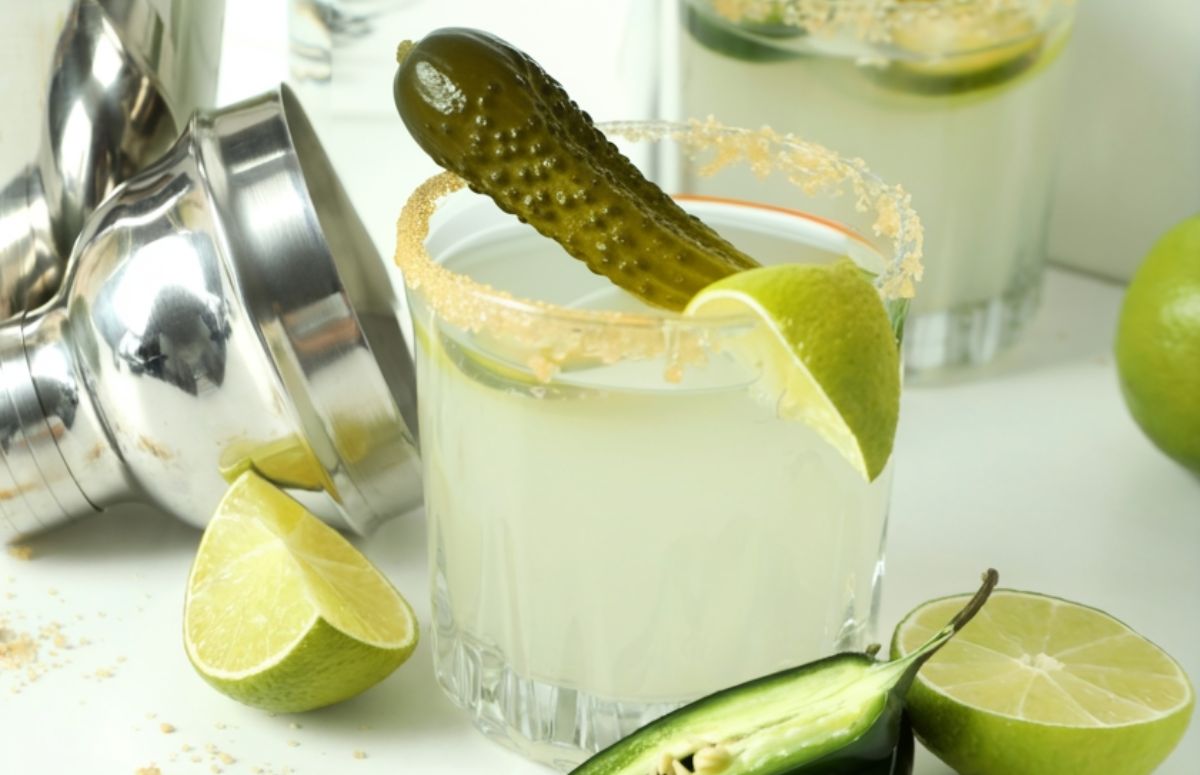 spicy pickle margarita in a glass next to a muddler