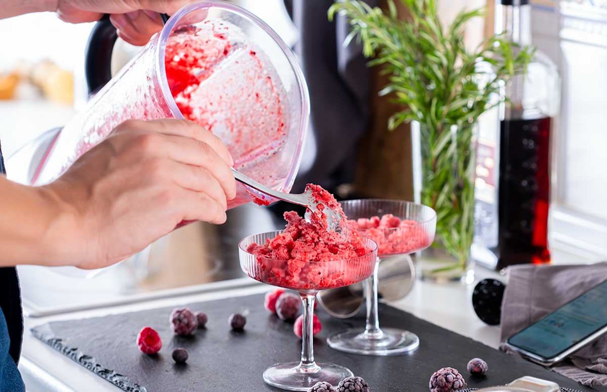 Pouring a frozen berry margarita into a glass from the blender