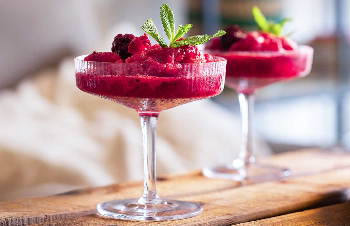 two raspberry frozen margaritas in tall stem glasses