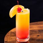 frozen tequila sunrise in a tall glass with fruit garnishes