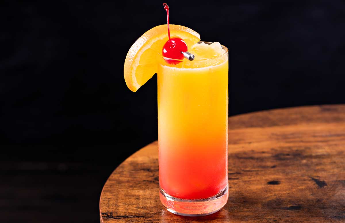 frozen tequila sunrise in a tall glass with fruit garnishes