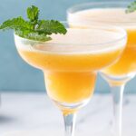 two frozen peach margaritas in long stem margarita glasses